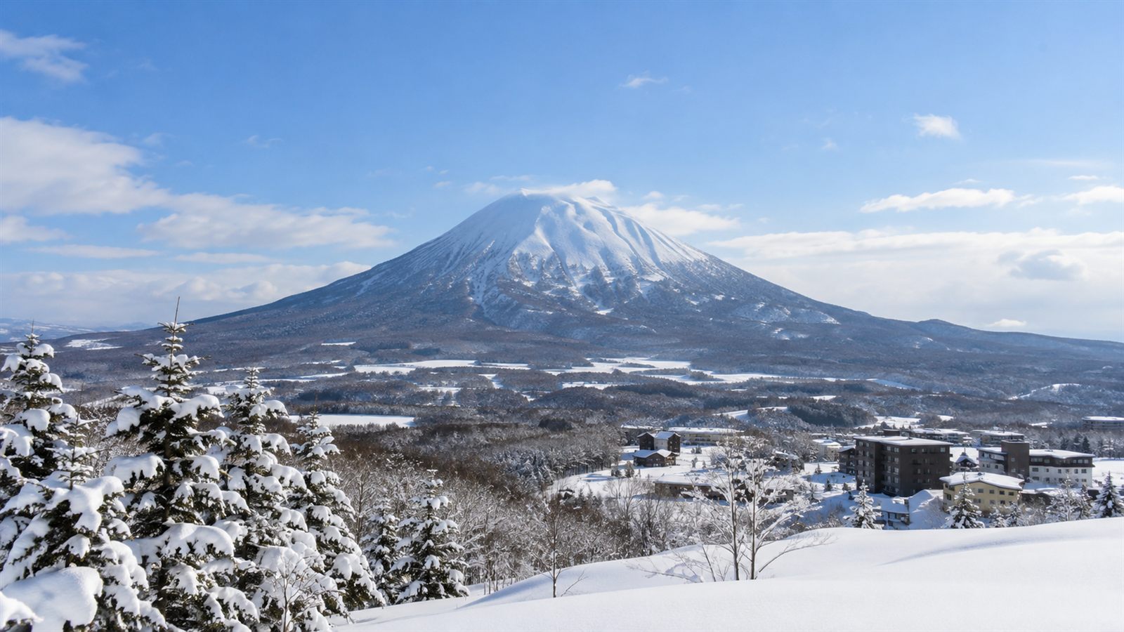 冬のニセコ。雪をかぶった羊蹄山とふもとの宿泊施設